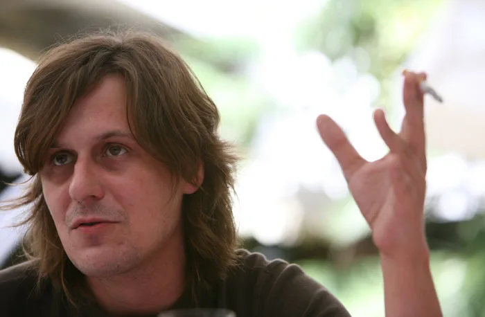 Retrato de Nacho Vegas con el pelo largo, gesticulando con un cigarrillo en la mano mientras habla