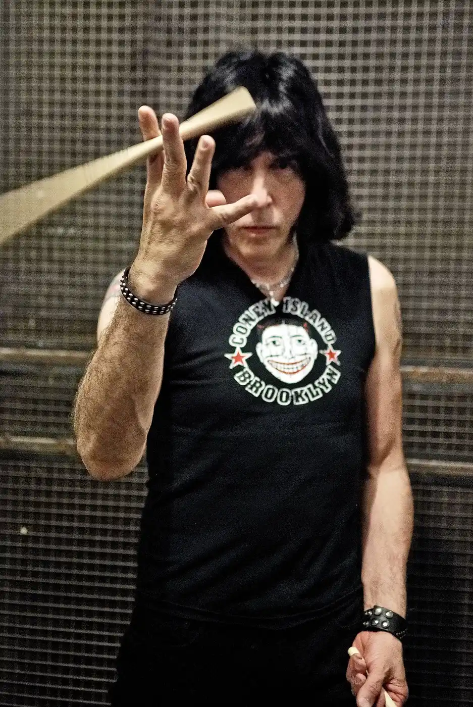 Retrato de Marky Ramone haciendo el gesto de cuernos con una baqueta en la mano