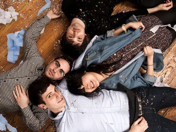 Los cuatro integrantes de The Pains of Being Pure at Heart recostados en el suelo de un living, rodeados de papel picado