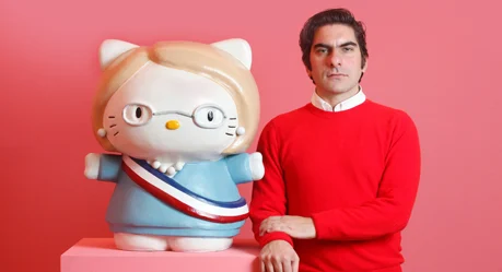 El artista uruguayo Martín Sastre, de suéter rojo, junto a su escultura de una Hello Kitty vestida de Michelle Bachelet, sobre fondo rosado