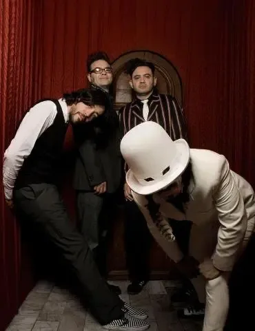 Los cuatro integrantes de Café Tacvba posando en un salón con cortinas rojas