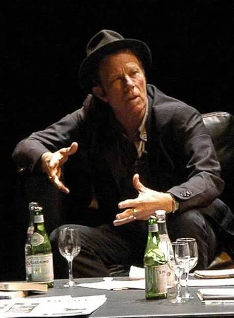 Tom Waits gesticulando con las manos durante una conversación sobre un escenario